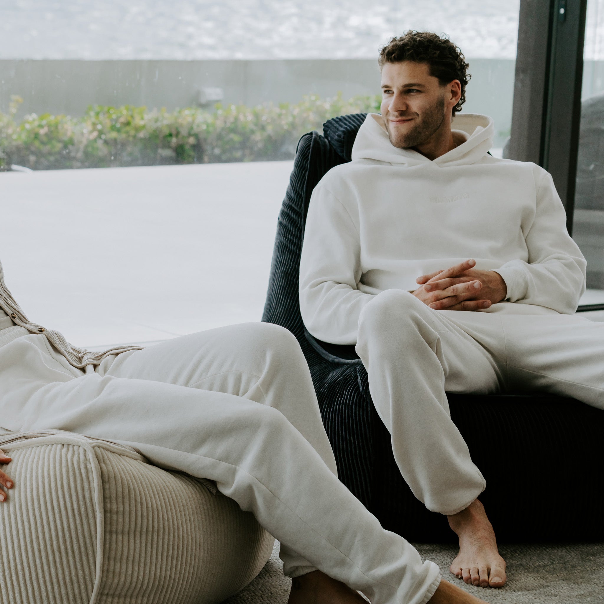 Man sitting on a cozy black ambient lounge calmera corduroy bean bag chair in the UK wearing a white hoodie and pants next to his girlfriend